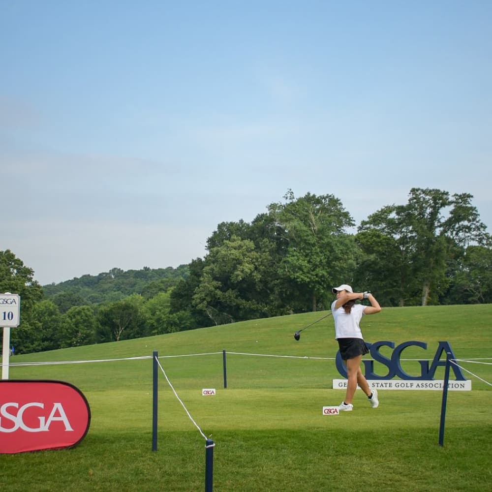 Golfer in white teeing off with a GSGA sign in the background