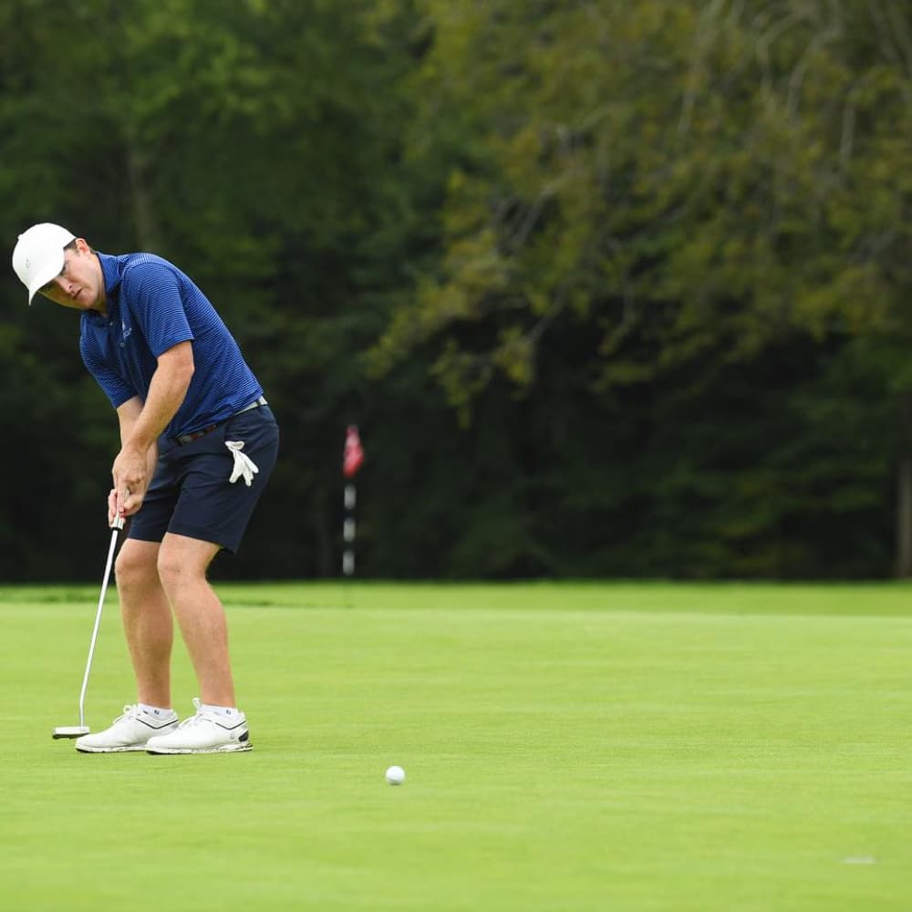 Golfer in white and blue attire putting on the green